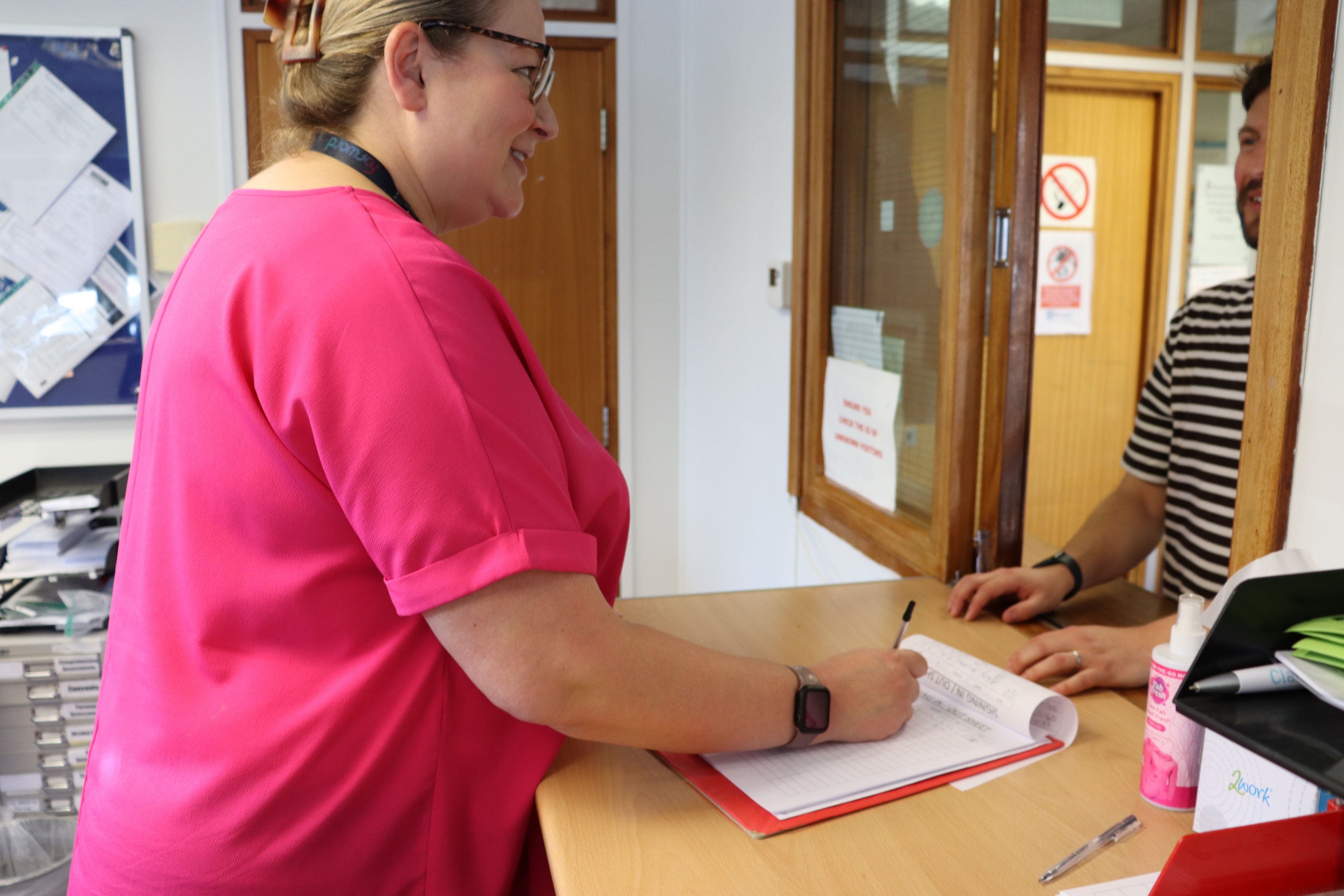 A lady signing a form on a clipboard at a reception desk